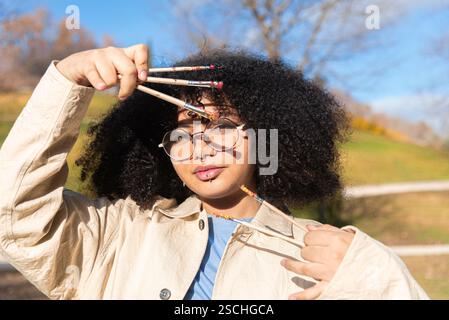 Un jeune artiste noir créatif tenant plusieurs pinceaux à l'extérieur, entouré par la nature. La jeune femme exprime l'individualité et la créativité, sho Banque D'Images