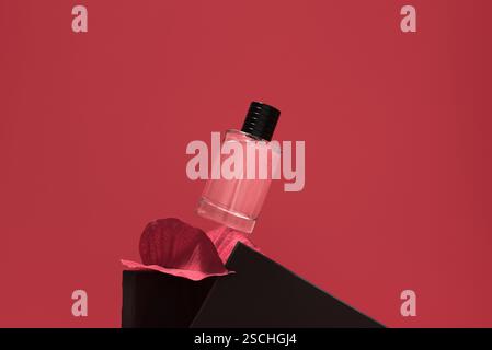 Une bouteille de parfum élégante repose élégamment sur des pierres noires, sur un fond rouge vif. La composition met en valeur l'esthétique moderne et le luxe. Banque D'Images