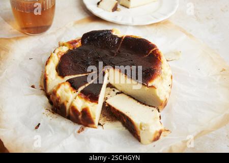 L'image de haute qualité capture un cheesecake de Saint-Sébastien fraîchement cuit, avec son dessus brûlé caractéristique et son intérieur crémeux, présenté sur parchme Banque D'Images