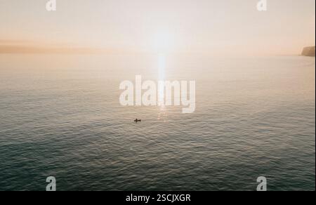 Un homme dans un canoë flotte sur l'océan. Le ciel est orange et l'eau est calme Banque D'Images