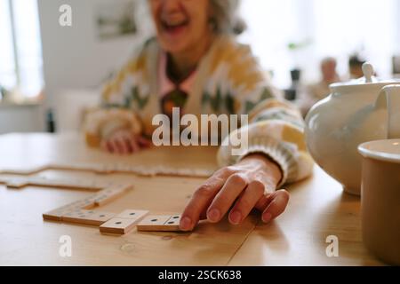 Gros plan moyen de la main féminine posant la tuile de domino tout en jouant au jeu de société dans la maison de retraite Banque D'Images