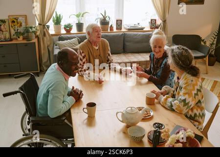 Plan à angle élevé de la compagnie biraciale d'amis âgés assis à la table discutant et profitant de l'heure du thé Banque D'Images
