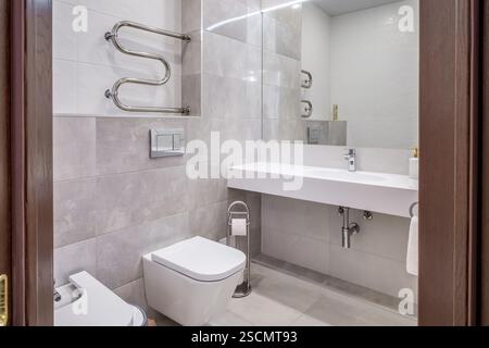 Salle de bains lumineuse et élégante avec douche vitrée, toilettes murales et carrelage effet marbre pour un look élégant et luxueux. Banque D'Images