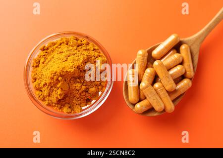 Capsules de curcuma dans une cuillère en bois et poudre sur fond orange, pose à plat Banque D'Images