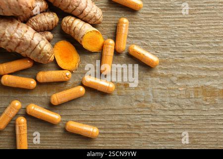 Capsules de curcuma en cuillère et racines sur table en bois, pose à plat. Espace pour le texte Banque D'Images