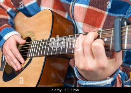 Personne jouant une guitare acoustique, portant une flanelle à carreaux. Main gauche sur la touche, strumming main droite. Capo attaché. Banque D'Images