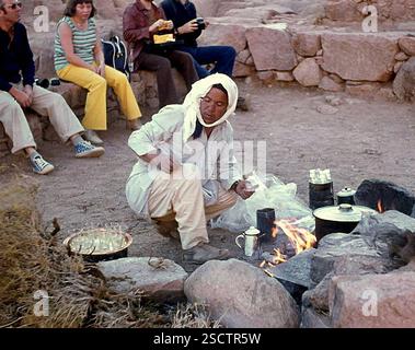Un bédouin fait du café sur un feu ouvert. Les touristes peuvent être vus en arrière-plan. [traduction automatique] Banque D'Images