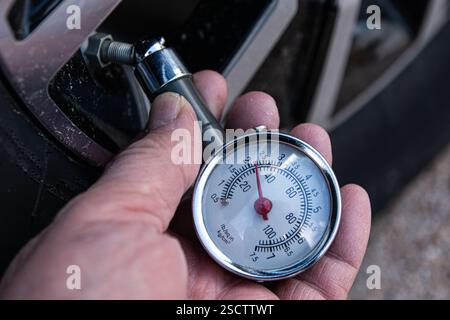 Un mécanicien vérifie la pression de sécurité des pneus d'une automobile à l'aide d'un manomètre. Banque D'Images
