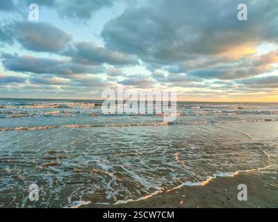 Un rivage paisible avec des vagues douces et un coucher de soleil vibrant se reflétant sur l'eau. Banque D'Images