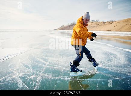Homme athlète en veste jaune patin sur glace sur le lac gelé avec des fissures et de la neige à l'heure d'hiver Banque D'Images