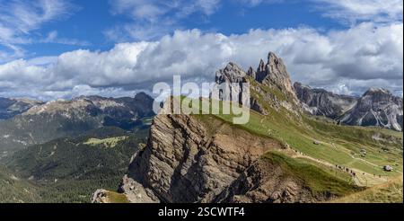 Large vue panoramique de Seceda, un lieu de photo renommé dans les Dolomites, Italie, avec un plateau herbeux, des falaises abruptes, des sommets montagneux et des touristes e. Banque D'Images