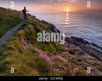 Walker regardant vers la mer depuis le sentier de la côte d'Anglesey au coucher du soleil au printemps, près de Cemaes, Anglesey, pays de Galles du Nord, Royaume-Uni Banque D'Images