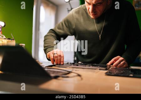 Vue à angle bas du technicien examinant attentivement et réparant la carte mère de l'ordinateur portable, dépannage des problèmes matériels assis à table dans l'atelier. Banque D'Images