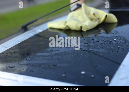 Main avec un gant jaune essuyant une surface mouillée sur une voiture Banque D'Images