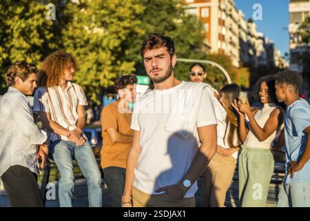 Portrait d'un jeune étudiant occasionnel sérieux de caucascien debout avec des amis à la ville pendant le soleil Banque D'Images