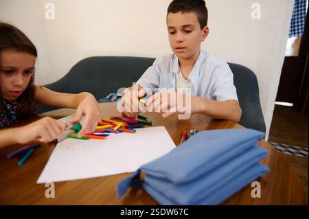 Deux enfants se livrant à une activité artistique et artisanale, utilisant des crayons colorés sur papier. Ce moment intérieur dépeint la créativité, la concentration et le lear jeune Banque D'Images