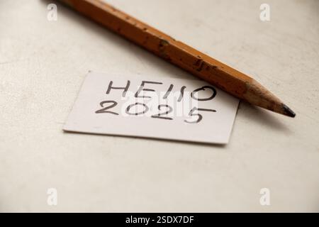 Bonjour 2025 écrit sur un morceau de papier et un crayon couché sur la table, pour saluer la nouvelle année Banque D'Images