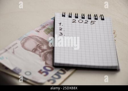 2025 et 123 écrit dans un cahier et ukrainien 50 hryvnia qui est couché sur la table, les plans pour la nouvelle année, écrire des plans Banque D'Images