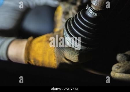 Vue rapprochée des mains en gants manipulant un joint homocinétique et un essieu sur une voiture Banque D'Images