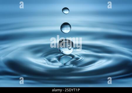 Trois gouttes claires tombant dans l'eau bleue et faisant des ondulations, prise de vue en studio Banque D'Images