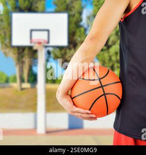 Vue arrière rognée d'un joueur de basket-ball tenant un ballon de basket-ball contre à l'extérieur Banque D'Images
