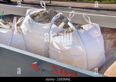 Sacs dans un grand conteneur en acier rouillé chargé de fragments de béton et de pierres de construction Banque D'Images