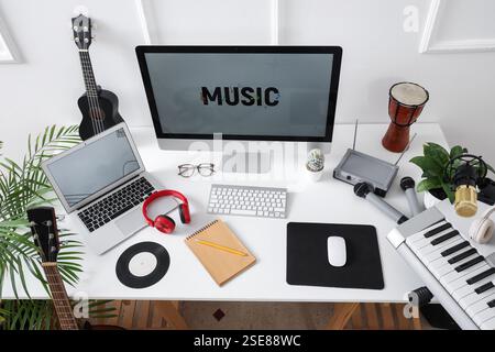 Lieu de travail avec ordinateur et instruments de musique près du mur lumineux dans le studio, vue de dessus Banque D'Images