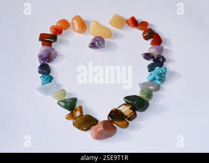 Collection de diverses pierres précieuses minérales brutes comme l'oeil de tigre, l'améthyste, la citrine, le quartz, le jaspe, malachite, placé dans une forme de coeur sur fond blanc Banque D'Images