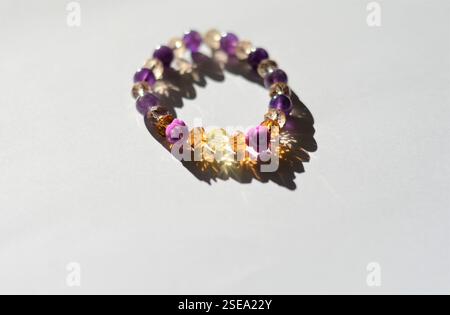 bracelet perlé fait à la main avec perles en forme de rose violet, ambre et rose, élégamment affiché sur un fond blanc avec des reflets de lumière naturelle Banque D'Images