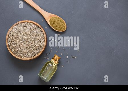 Bouteille de verre de graines de Caraway huile essentielle avec de la poudre de caraloin dans une cuillère en bois sur une table rustique ( Cluminum cyminum ) Banque D'Images