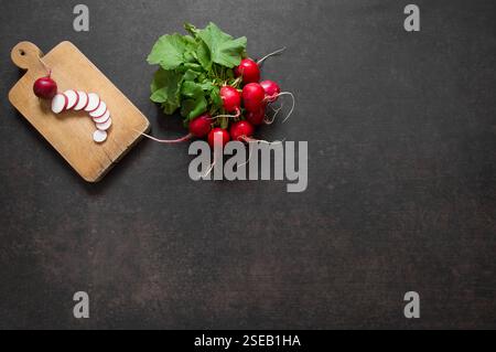 Grappe récoltée de radis rouges crus frais avec feuille près de la planche à découper sur radis tranchés. Légume biologique sain ( Raphanus sativus ) Banque D'Images