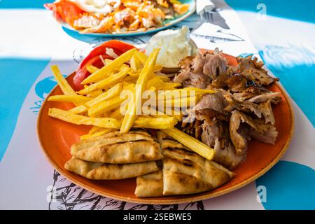 Assiette avec viande Gyros, pain pita, tomates et frites sur table dans un restaurant grec, port Adamas, île de Milos, Cyclades, Grèce Banque D'Images