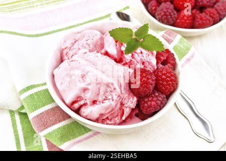 La crème glacée à la framboise rouge et menthe baies en blanc bol, une cuillère sur serviette sur planche de bois contexte Banque D'Images