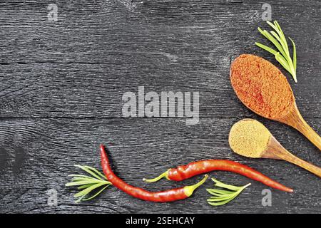 Image de branches de romarin frais, gousses de piment rouge et deux cuillères avec moulu sur une planche en bois au-dessus de l'arrière-plan Banque D'Images