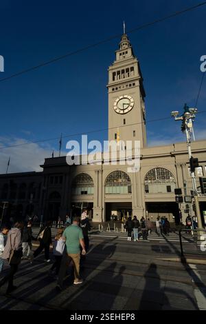 Les piétons traversent la rue en face du Ferry Building, San Francisco, CA, avec l'emblématique tour de l'horloge du Ferry Building visible. Banque D'Images