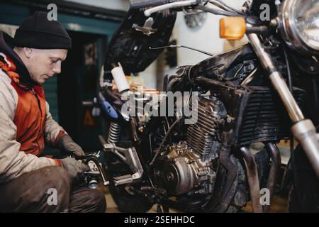 Mécanicien concentré sur la réparation de moto, examinant le moteur dans un atelier Banque D'Images