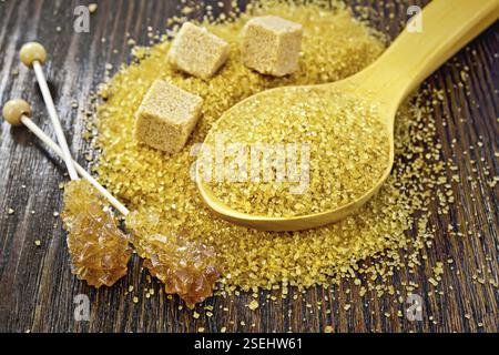 Le sucre granulé brun dans une cuillère, cubes et cristal sur un bâton contre un conseil en bois foncé Banque D'Images