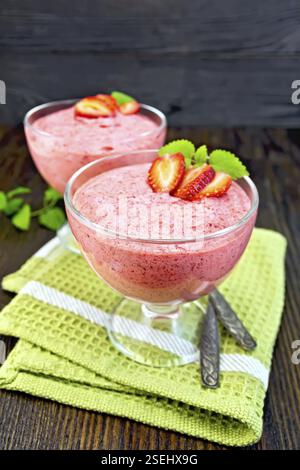 Fraise gelée dans l'air deux cuillères, bols en verre sur une serviette verte, menthe sur fond de planches en bois Banque D'Images