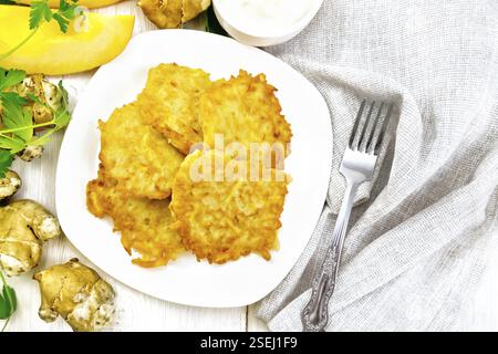 Beignets de topinambours de citrouille dans une assiette, la crème dans un bol, serviette, le persil et la fourche sur planche de bois au-dessus de l'arrière-plan Banque D'Images