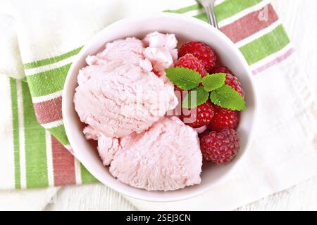 La crème glacée à la framboise rouge et menthe baies en blanc bol, une cuillère sur planche de bois serviette de fond ci-dessus Banque D'Images