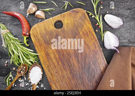 Cadre de l'aneth, des cuillères en bois avec des pois de poivre et sel, branches de romarin frais, gousses de piment rouge, tranches d'ail, oignons et une serviette sur Banque D'Images