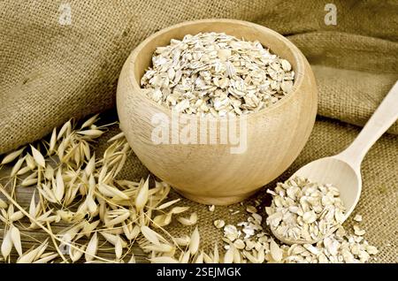 Flocons d'avoine dans un bol en bois avec cuillère, tiges d'avoine sur toile de jute et planche de bois Banque D'Images