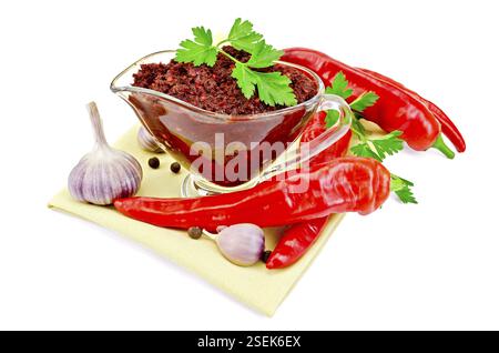 Tabasco dans un bateau de sauce en verre avec du poivron rouge frais, du persil et de l'ail sur une serviette jaune sur un fond blanc Banque D'Images