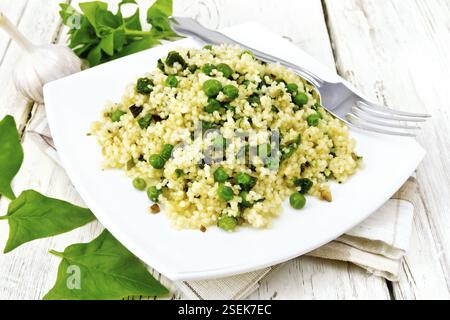 Couscous aux épinards et les petits pois dans une assiette sur une serviette de cuisine, le basilic et la fourche sur une planche en bois historique Banque D'Images