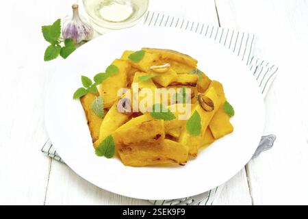 Potiron frit avec de l'ail, de la cannelle et du vinaigre dans une assiette sur une serviette, de l'huile et de la menthe sur fond de bois Banque D'Images