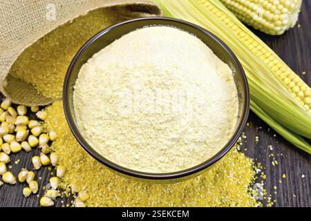 La farine de maïs dans un bol sur les libéraux, les épis et les grains, un sac sur un fond en bois foncé Banque D'Images