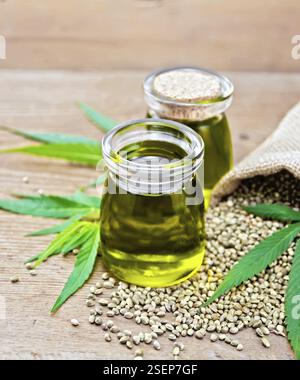 L'huile de chanvre dans deux pots en verre avec le grain dans le sac et sur la table, feuilles de cannabis sur l'arrière-plan d'une vieille planche de bois Banque D'Images