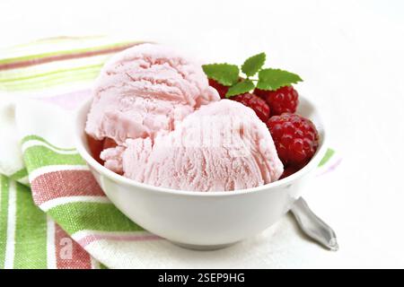 La crème glacée à la framboise rouge et menthe baies en blanc bol, une cuillère sur serviette sur le fond de carte en bois clair Banque D'Images