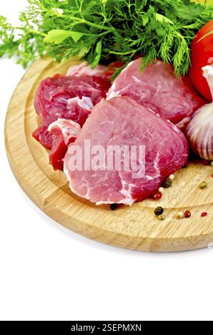 Viande tranchée, ail, tomates, persil, aneth sur une planche de bois ronde sur fond blanc Banque D'Images