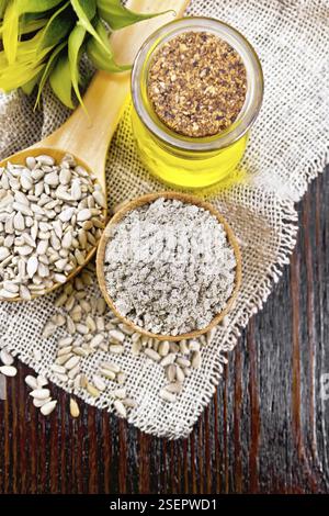 Farine de tournesol dans un bol, huile dans un pot en verre, graines dans une cuillère sur toile de jute, bourgeon de fleur de tournesol sur fond de planche en bois d'en haut Banque D'Images